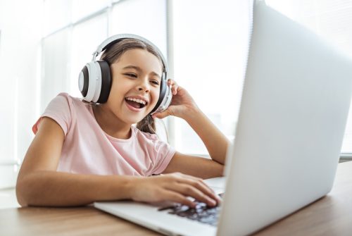 A happy girl in headphones with a laptop sitting at the table